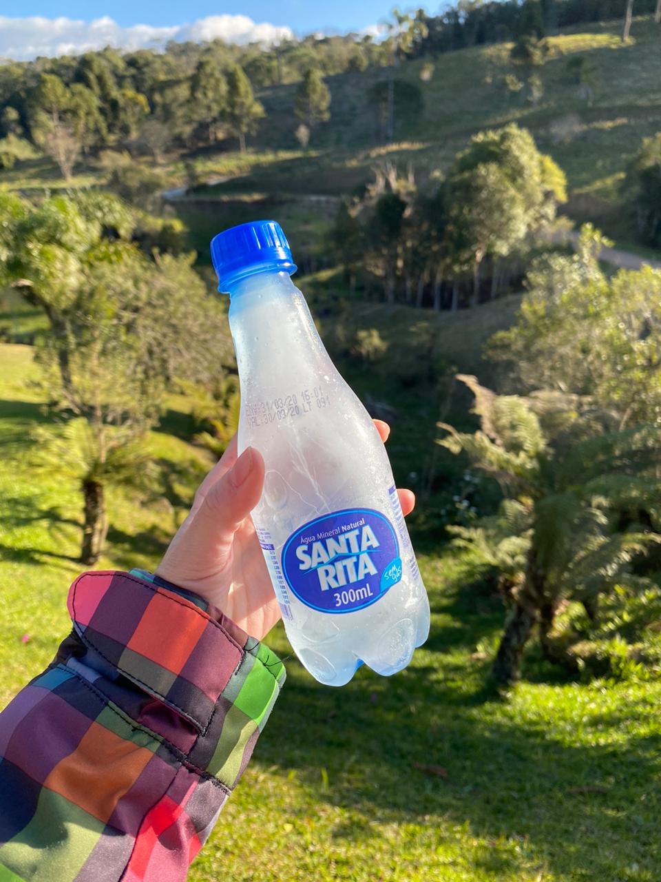 Garrafa de Água Santa Rita diante de uma paisagem verde não identificada