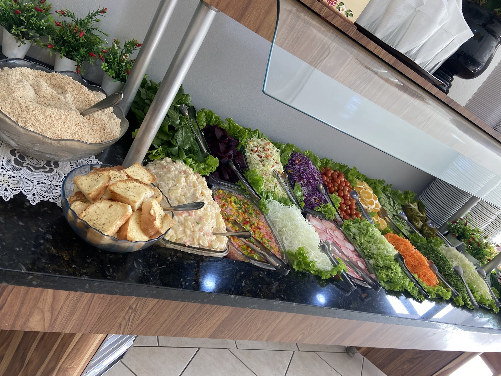 Balcão de saladas e acompanhamentos do Restaurante da Jane, com verduras, legumes, farofa e pães.